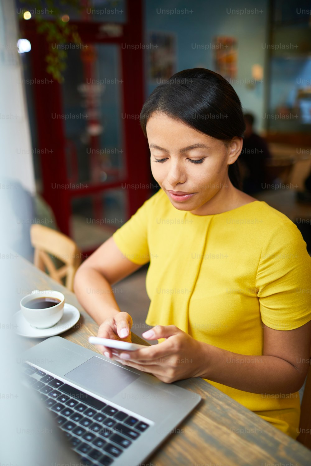Young businesswoman in smart casualwear messaging in smartphone in front of laptop