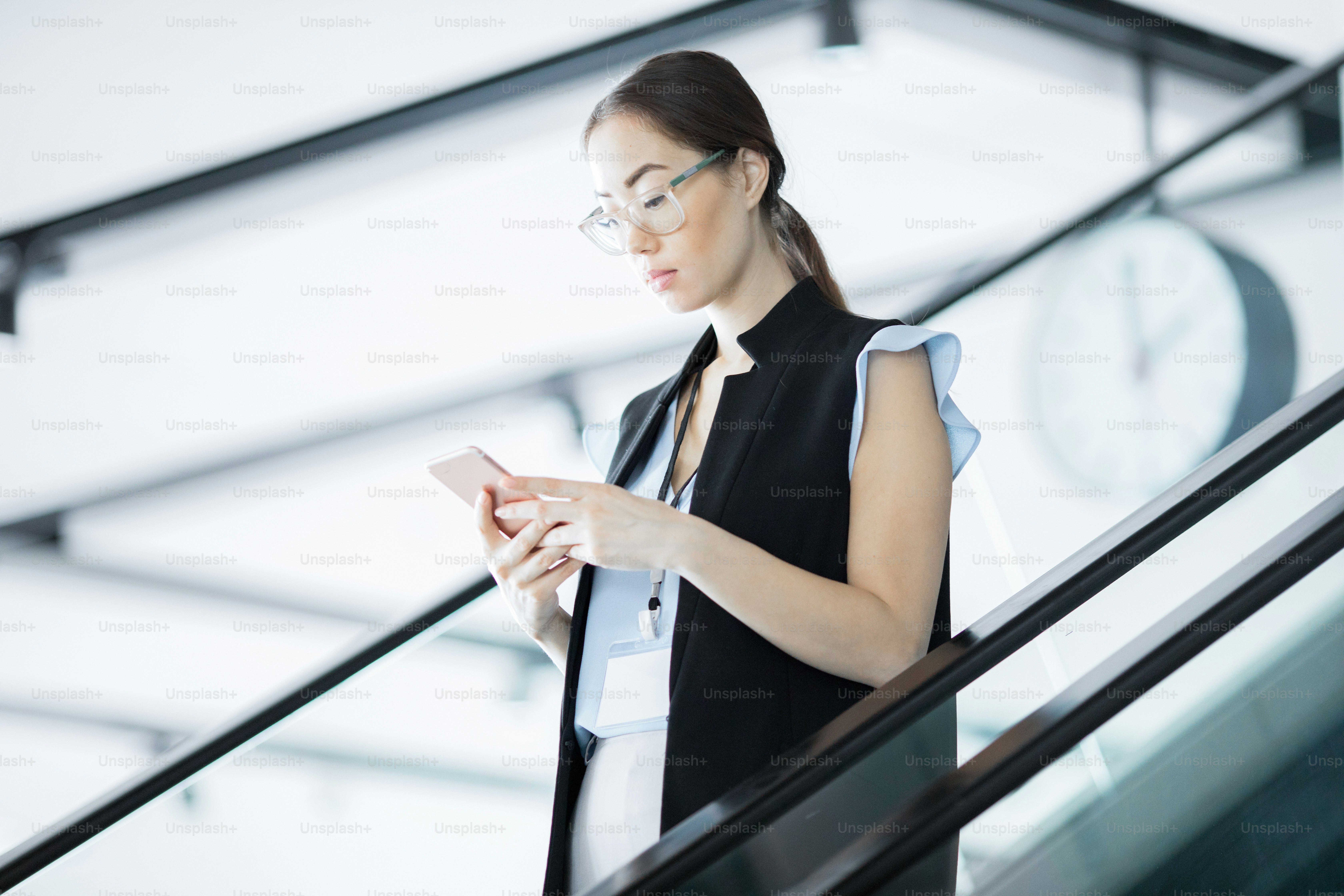 Vielbeschäftigter junger Teilnehmer der Konferenz liest Nachricht im Smartphone, während er sich auf der Rolltreppe bewegt