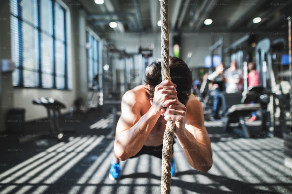 Junger fitter Mann, der im Fitnessstudio trainiert. Ein Junge in einer Planke, der sich an einem Kletterseil festhält.