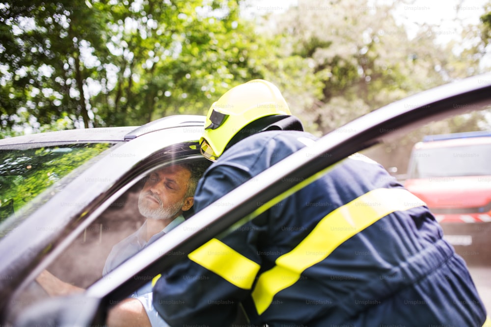 Um bombeiro irreconhecível tirando um homem inconsciente do carro após um acidente.