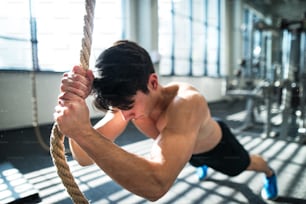 Young fit man working out in gym. A boy in a plank holding onto a climbing rope.