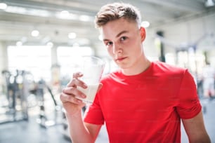 Un giovane in forma in palestra che tiene un bicchiere con una bevanda proteica. Copia spazio.