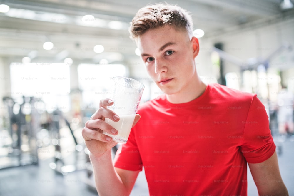 A young fit men in gym holding a glass with protein drink. Copy space.