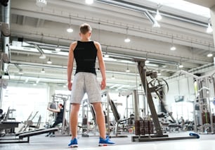 Young man in modern gym, standing. Rear view. Copy space.