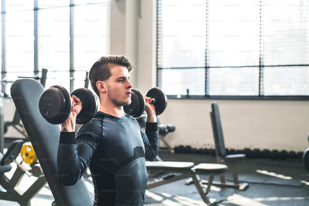 Young fit men doing strength training, exercising with dumbbells in modern gym. Copy space.