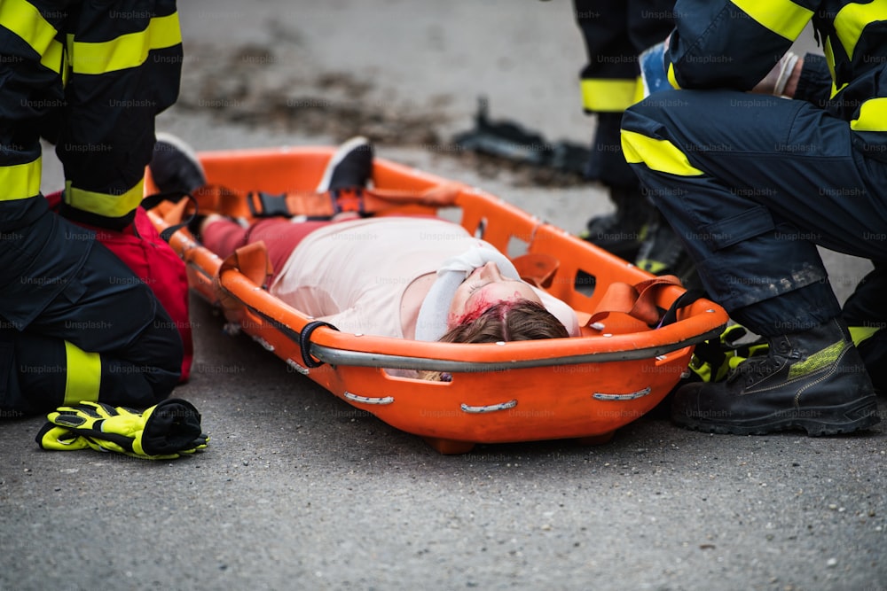 Vigili del fuoco irriconoscibili che mettono una giovane donna ferita in una barella di plastica sulla strada dopo un incidente d'auto. Primo piano.