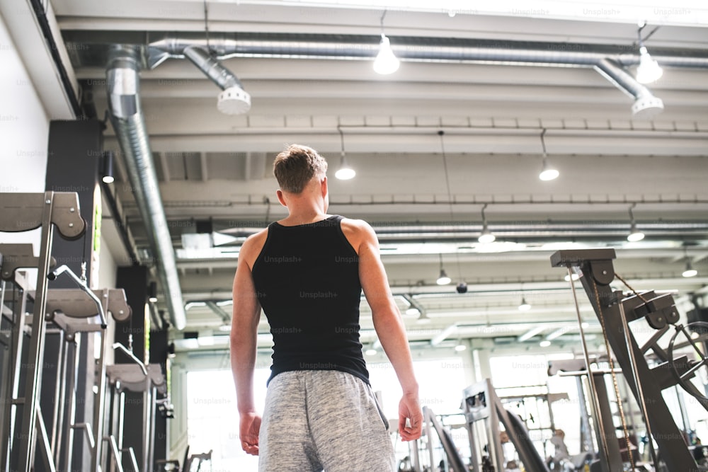Young man in modern gym, standing. Rear view. Copy space.