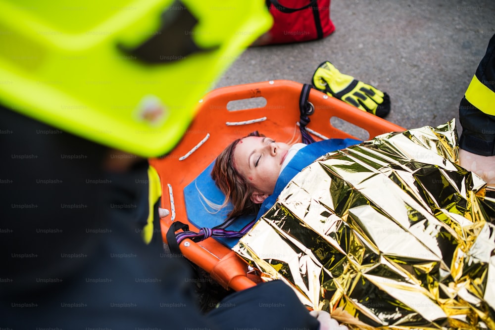 Uma jovem mulher ferida em uma maca de plástico após um acidente de carro, coberta por cobertor térmico. De perto.
