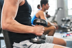 Unrecognizable young fit men doing strength training, exercising with dumbbells in modern gym.