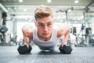 Fit man doing strength training, doing push ups on dumbbells in modern gym. Close-up.