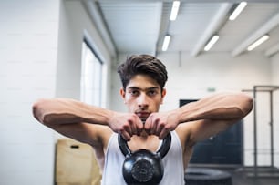 Fit hispanic man doing strength training, lifting kettlebell in gym gym.