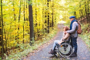 Active senior couple on a walk in a beautiful autumn nature. A man and woman in a wheelchair in a forest.