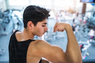 A close up of a young handsome man in gym gym, standing and showing muscles.