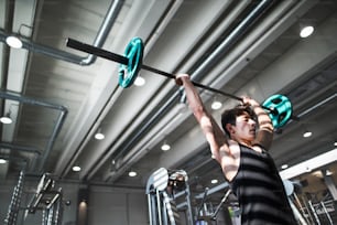 Young handsome fit man in gym working out, lifting bar of barbell, flexing muscles.