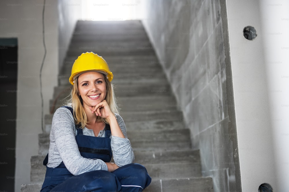 Young woman worker with a yellow helmet sitting on the stairs on the construction site. Copy space.
