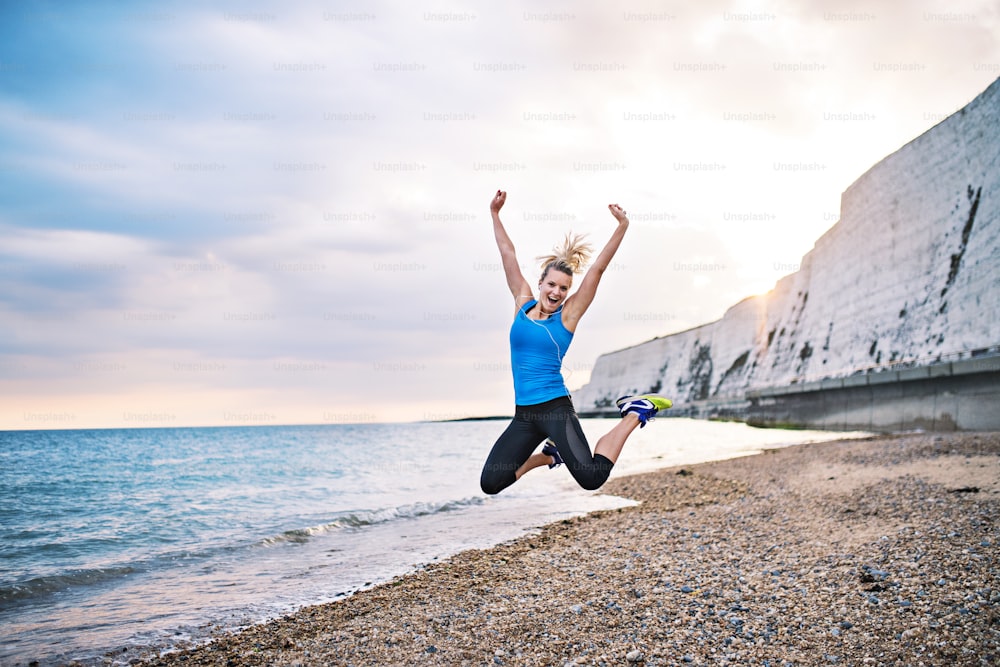 Young sporty woman runner in blue sportswear jumping outside on the beach in nature. Copy space.