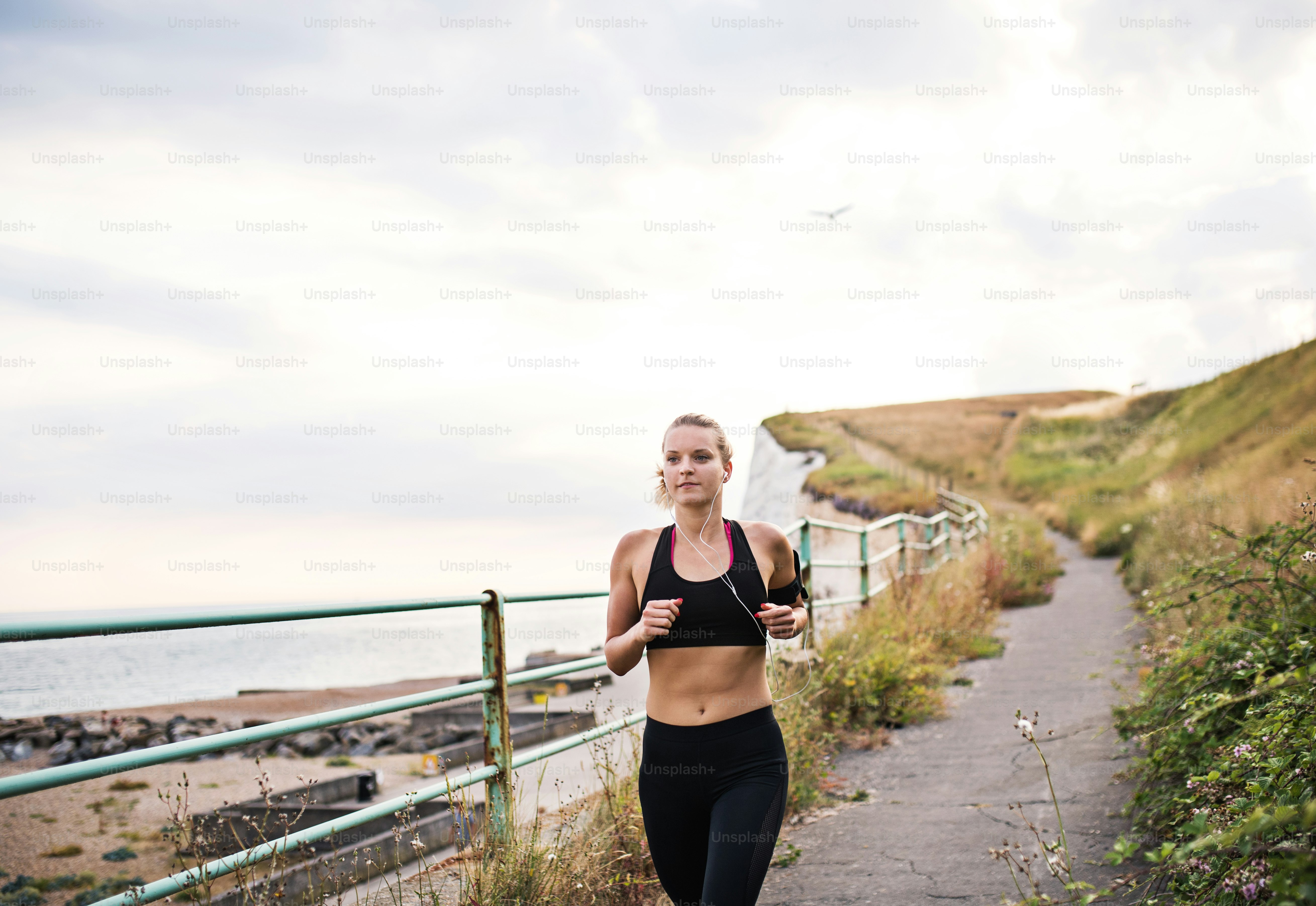 Jeune coureuse sportive avec des écouteurs courant au bord de la mer dans la nature, en écoutant de la musique.