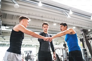 Young man friends standing and talking in modern gym gym, making fist bump.