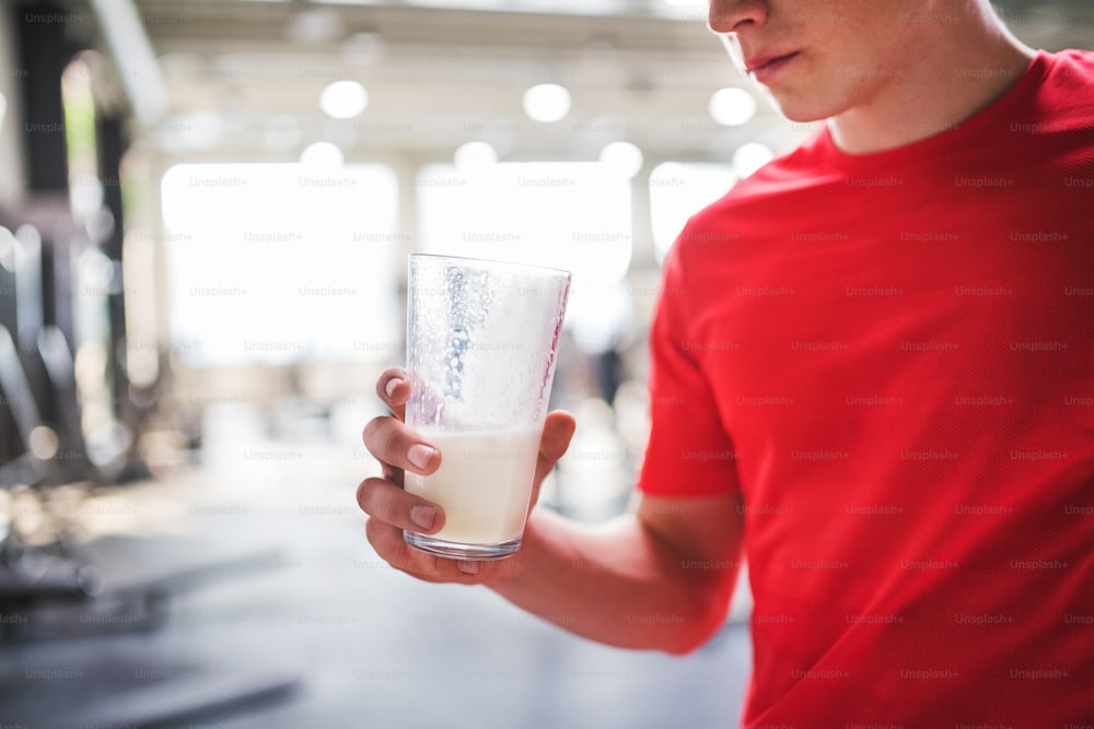 Ein nicht wiederzuerkennender junger fitter Mann im Fitnessstudio hält ein Glas mit Proteingetränk in der Hand. Speicherplatz kopieren.