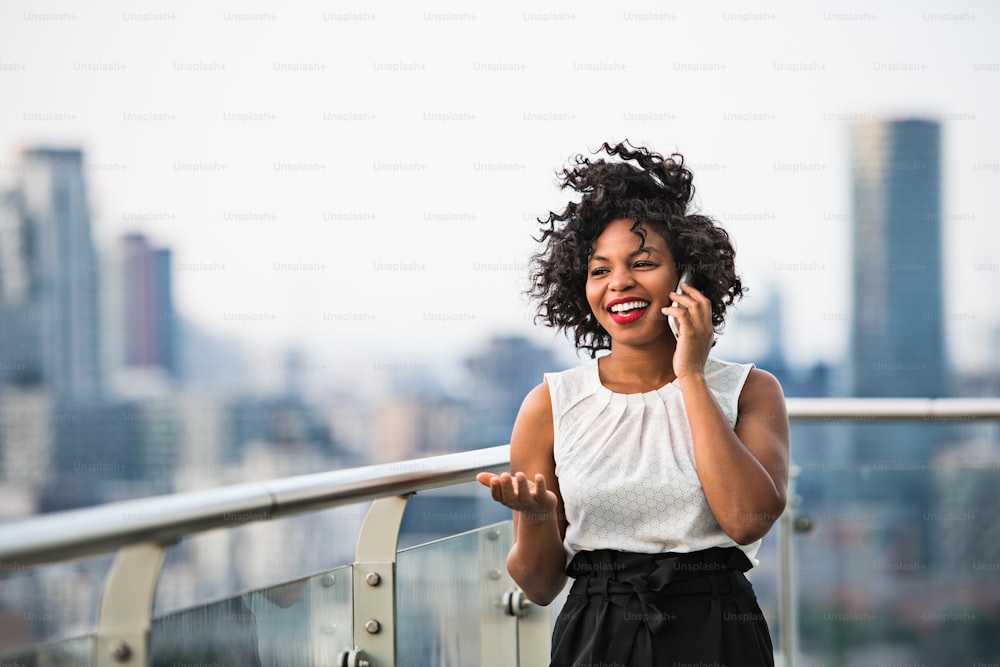A portrait of black businesswoman standing against London rooftop view panorama, making a phone call. Copy space.