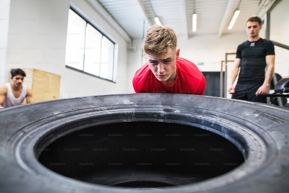Fit young man with his friends in gym working out, moving large tire.