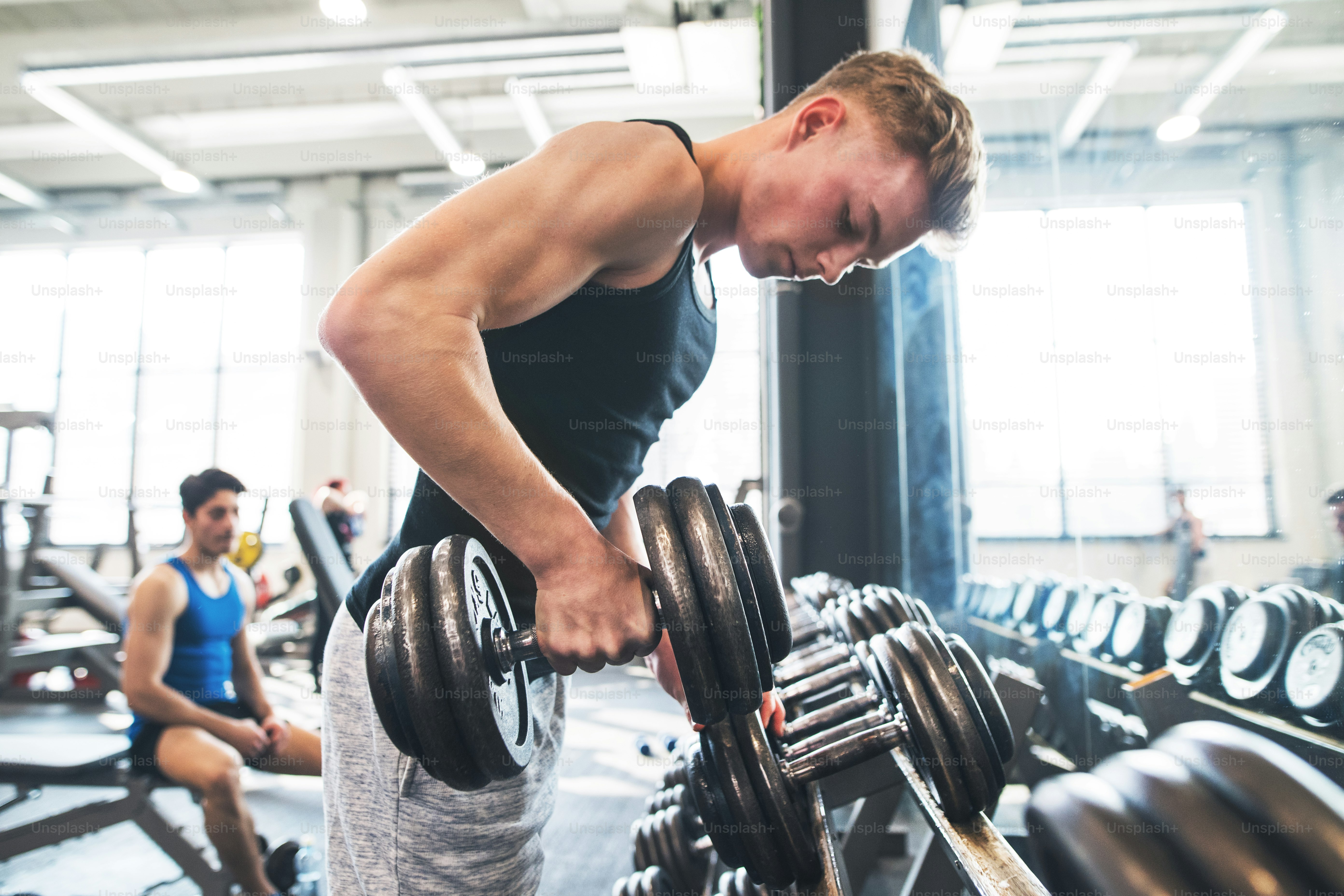 Young fit men doing strength training, exercising with dumbbells in ...