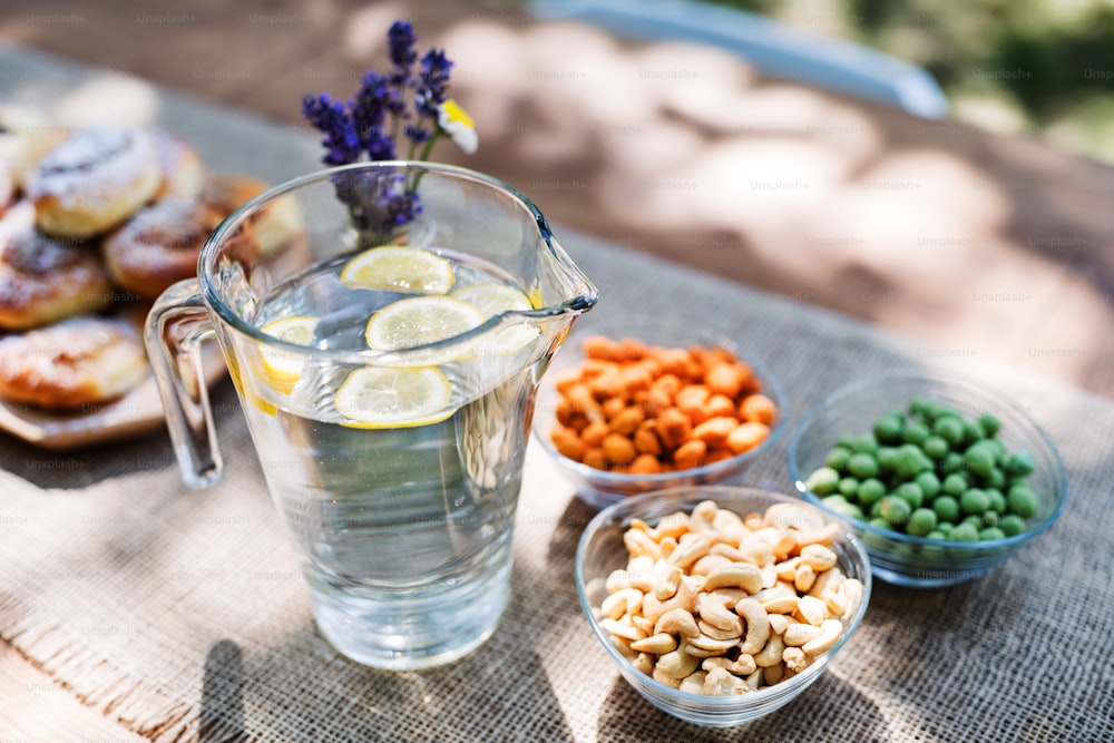 Primer plano de una mesa puesta para una fiesta en el jardín o una celebración al aire libre. Agua en una jarra, frutos secos y otros bocadillos salados en la mesa.