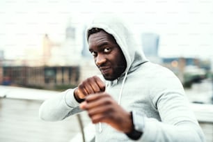 Gros plan d’un jeune sportif noir actif debout en position de boxe dans une ville.