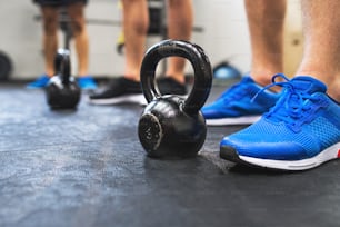 A close-up of legs of three fit men in gym standing by kettlebells.