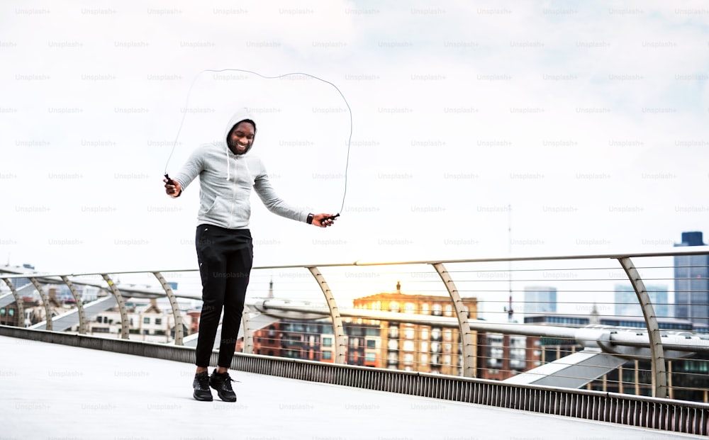 A close-up of a young active black sportsman skipping with a rope in a city, wearing hoodie. Copy space.