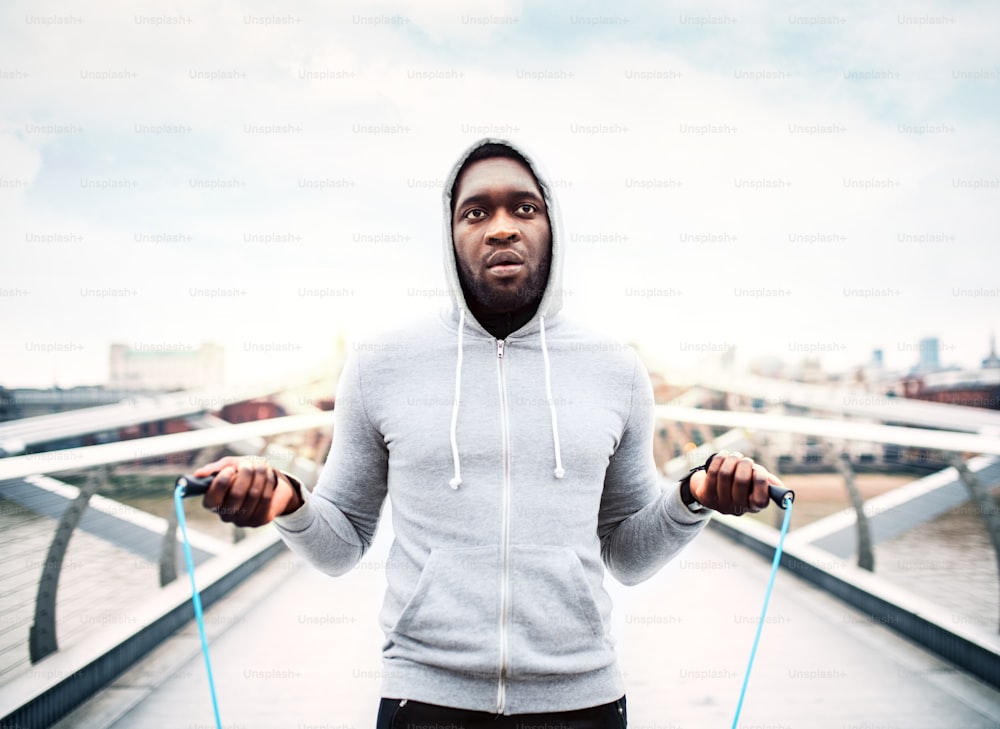 Young handsome active black sportsman skipping with a rope in a city, wearing hoodie.