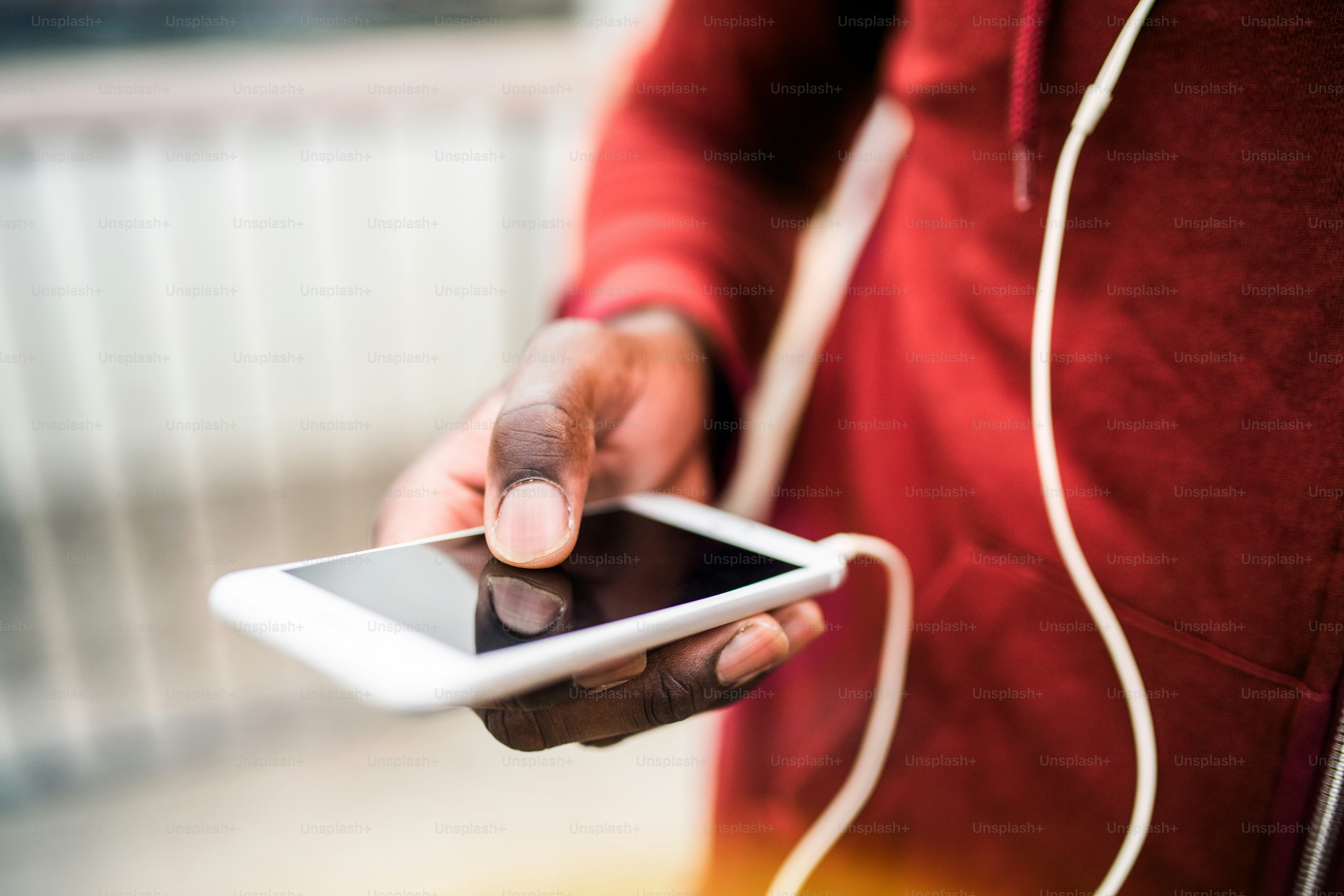 A close-up of an unrecognizable young sporty black man runner with smartphone and earphones before running outside in a city.