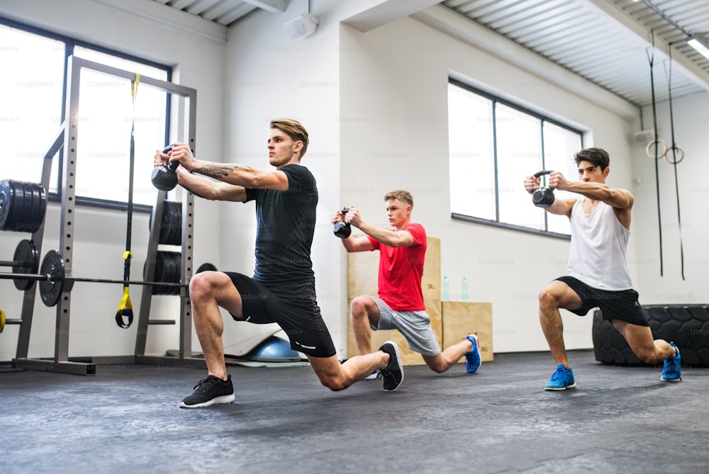 Drei junge fitte Männer im Fitnessstudio trainieren mit Kettlebells.