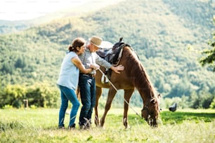 牧草地で草を食む馬を抱く幸せそうな老夫婦。