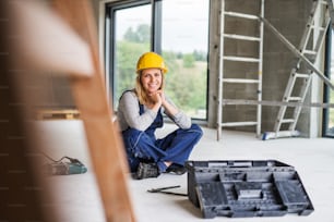 Portrait of a female worker on the construction site. Beautiful young woman sitting on the floor.