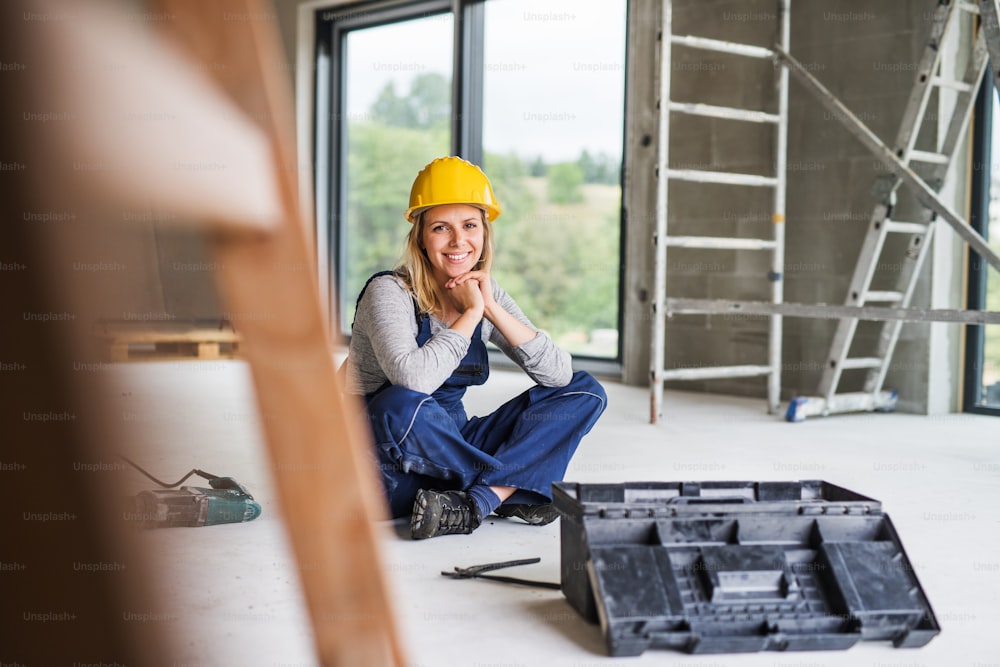 Portrait of a female worker on the construction site. Beautiful young woman sitting on the floor.