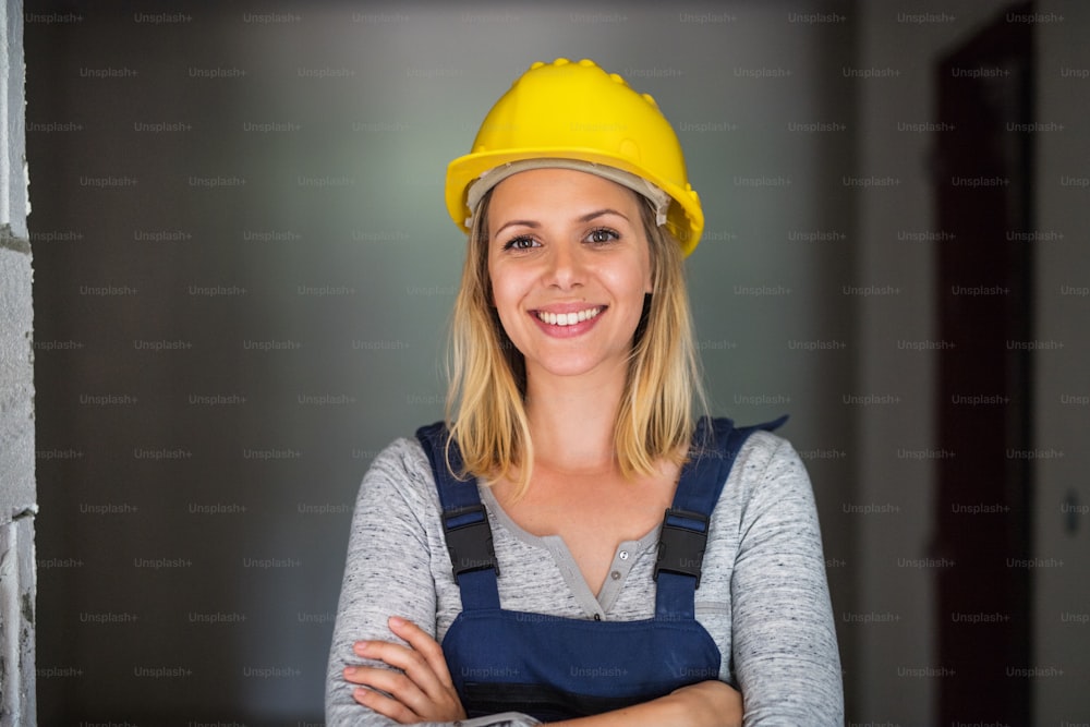Una trabajadora en la obra. Un retrato de cintura para arriba de una hermosa joven con un casco amarillo, con los brazos cruzados.