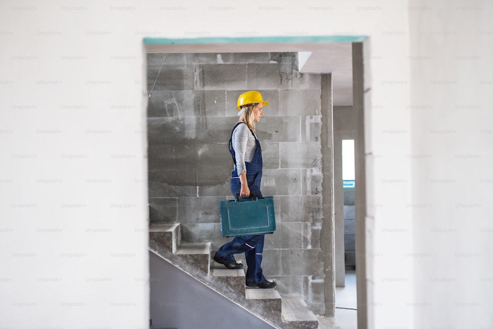 Young woman worker with a tool box walking down the stairs on the construction site. Copy space.
