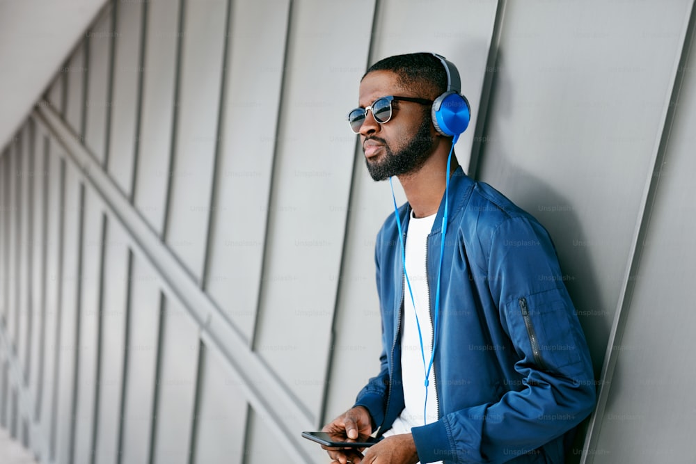 Fashion And Music. Man With Headphones And Phone In City. Fashionable Male Listening Music On Phone In Street. High Resolution
