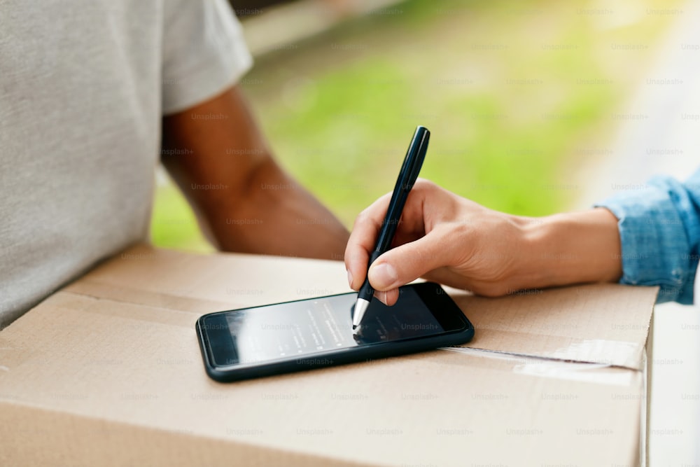 Package Delivery. Closeup Of Female Hand Signing On Phone On Box, Receiving Package From Courier. High Resolution