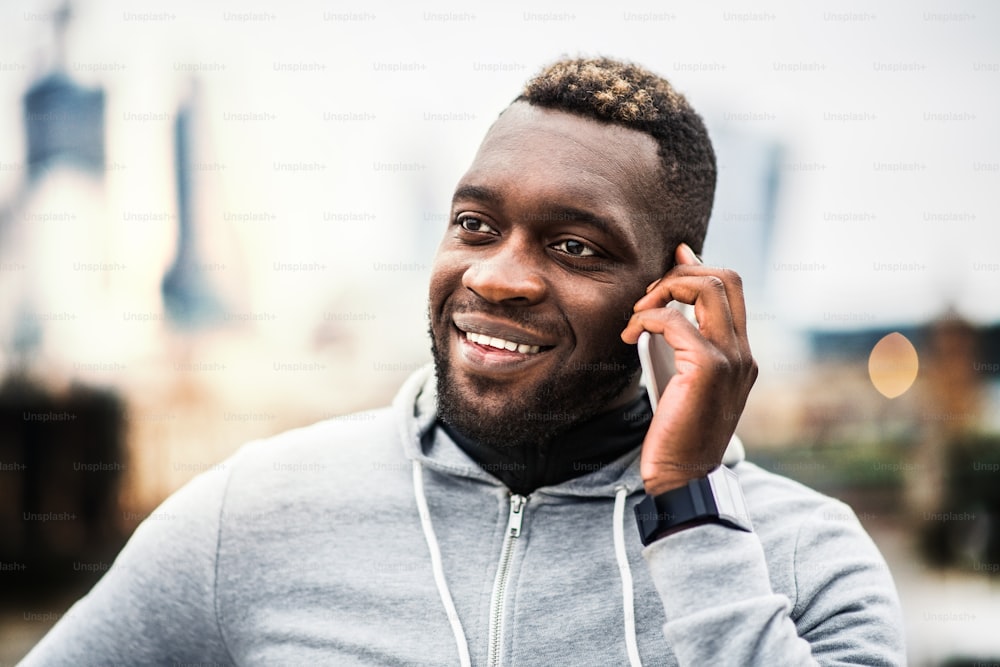 Young sporty black man runner with smartphone standing in a city, making a phone call. A close-up.
