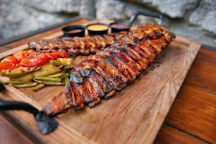 Food Closeup. Grilled Ribs In Barbecue Restaurant. Spareribs With Vegetables And Sauce On Wooden Tray. High Resolution