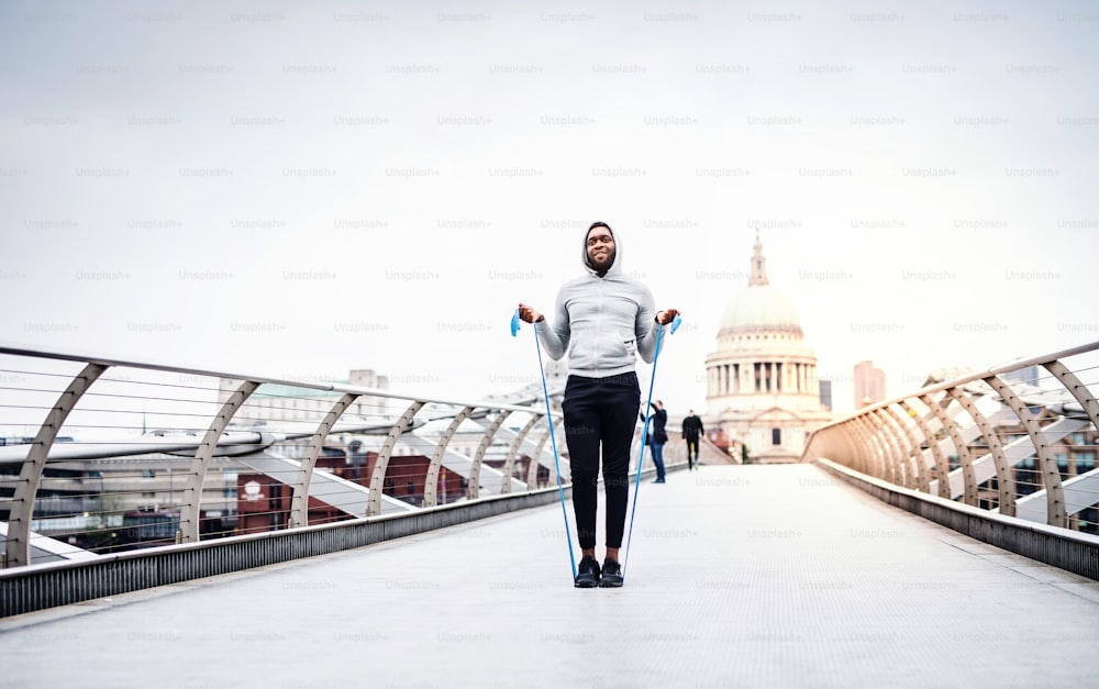 Young active black sportsman exercising with elastic rubber bands on the bridge in London, St.Paul's Cathedral in the background.