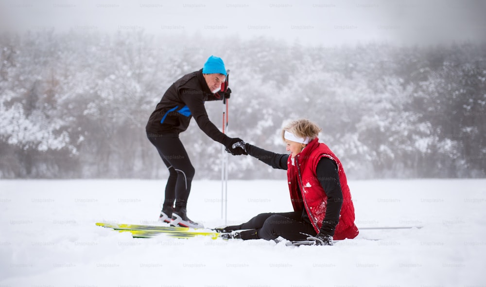 Active senior couple cross-country skiing. A man helping a woman to stand up. Winter time.