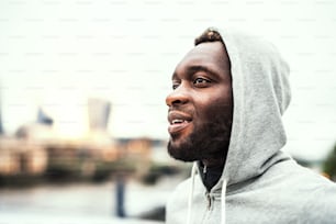 Close-up of a happy black man with gray hood on his head in a London city. Copy space.