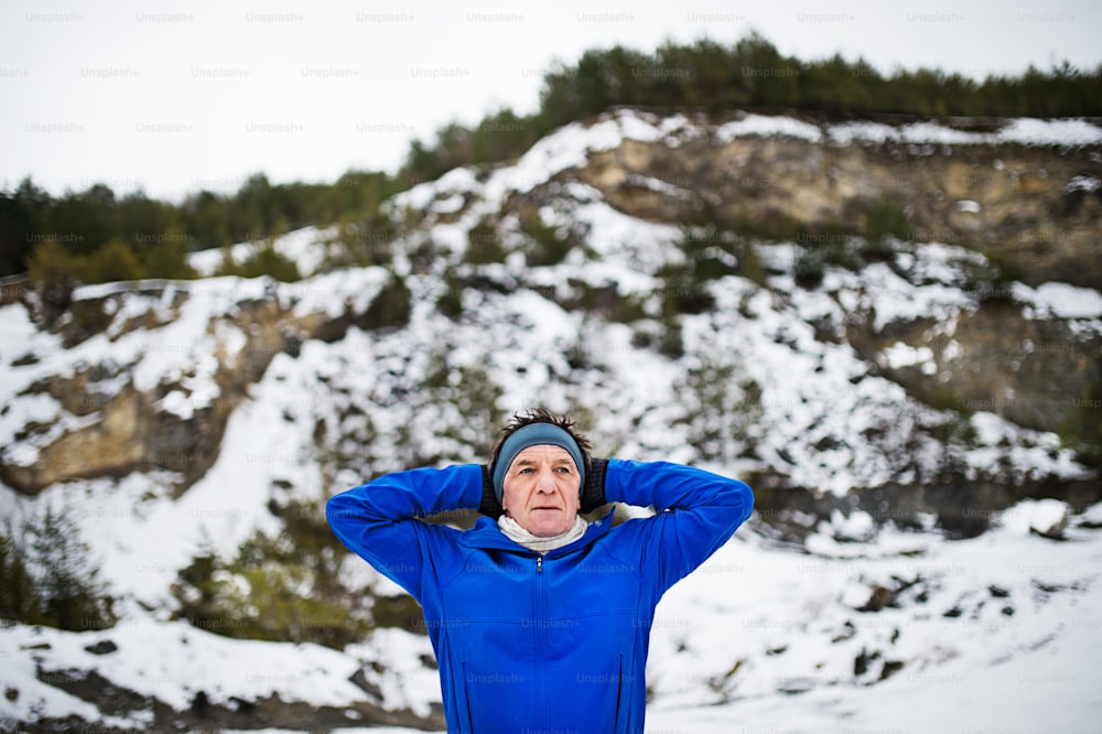 A waist-up portrait of senior man stretching before the run in winter nature. Copy space.