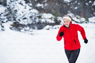 Senior woman jogging outside in winter nature. Copy space.