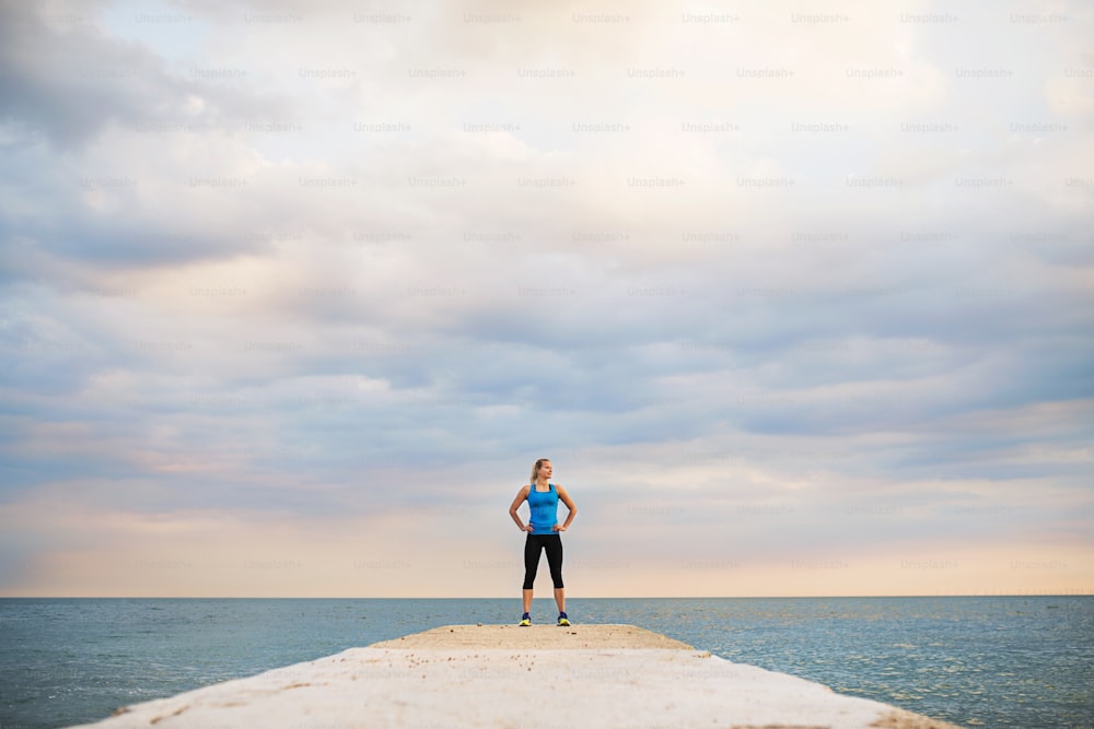 Eine junge sportliche Frau, die auf einem Pier steht, draußen am Meer. Speicherplatz kopieren.