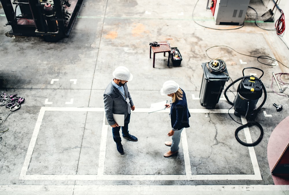 A high angle view of an industrial man and woman engineer with tablet in a factory, working.