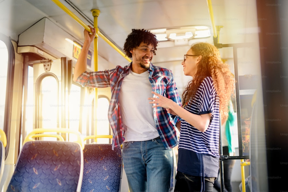 Giovane coppia carina in piedi in un autobus e parlando. Coppia di razza mista.